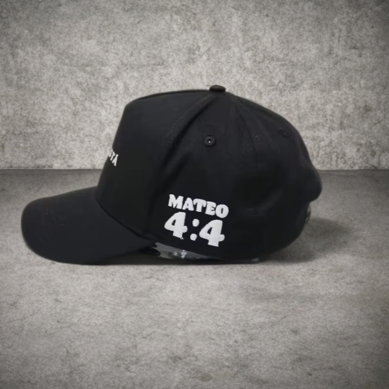 Black cap with 'MATEO 4:4' text on a gray surface and background